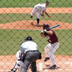 A baseball pitcher pitches to a batter in a game as the umpire looks on.