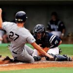 A baseball player wearing the number 27 slides safely into base.