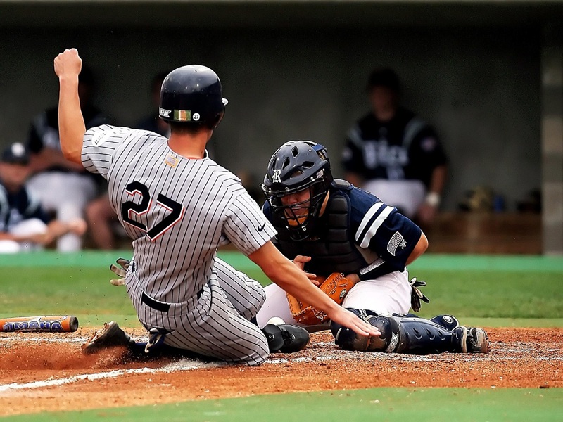A baseball player wearing the number 27 slides safely into base.
