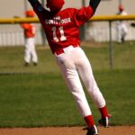 A baseball player leaps into the air to catch a ball going over his head.
