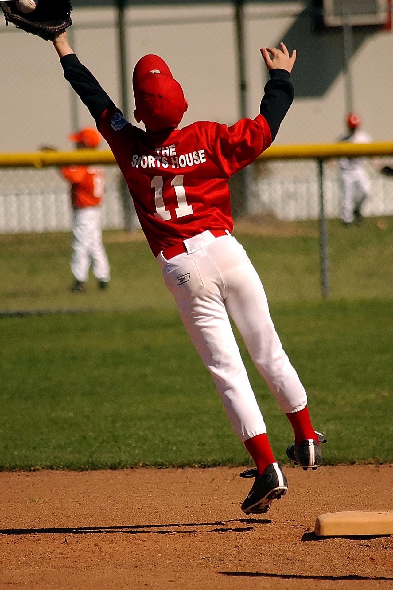 A baseball player leaps into the air to catch a ball going over his head.