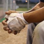 A baseball player sits alone in the dugout, clasping his hands.