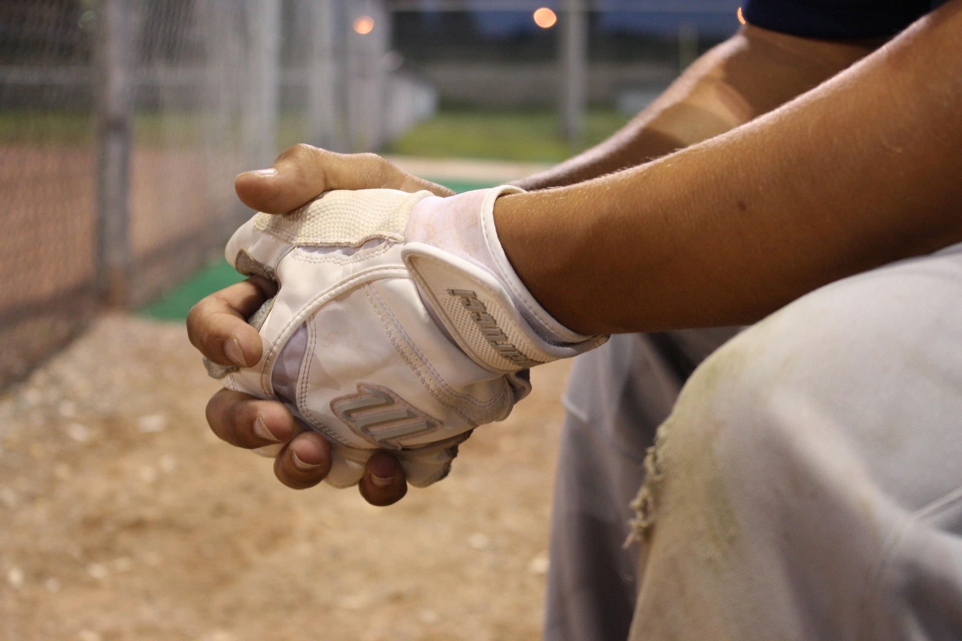 A baseball player sits alone in the dugout, clasping his hands.