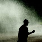 Silhouette of a pitcher on a baseball field with the sprinkler on behind him.