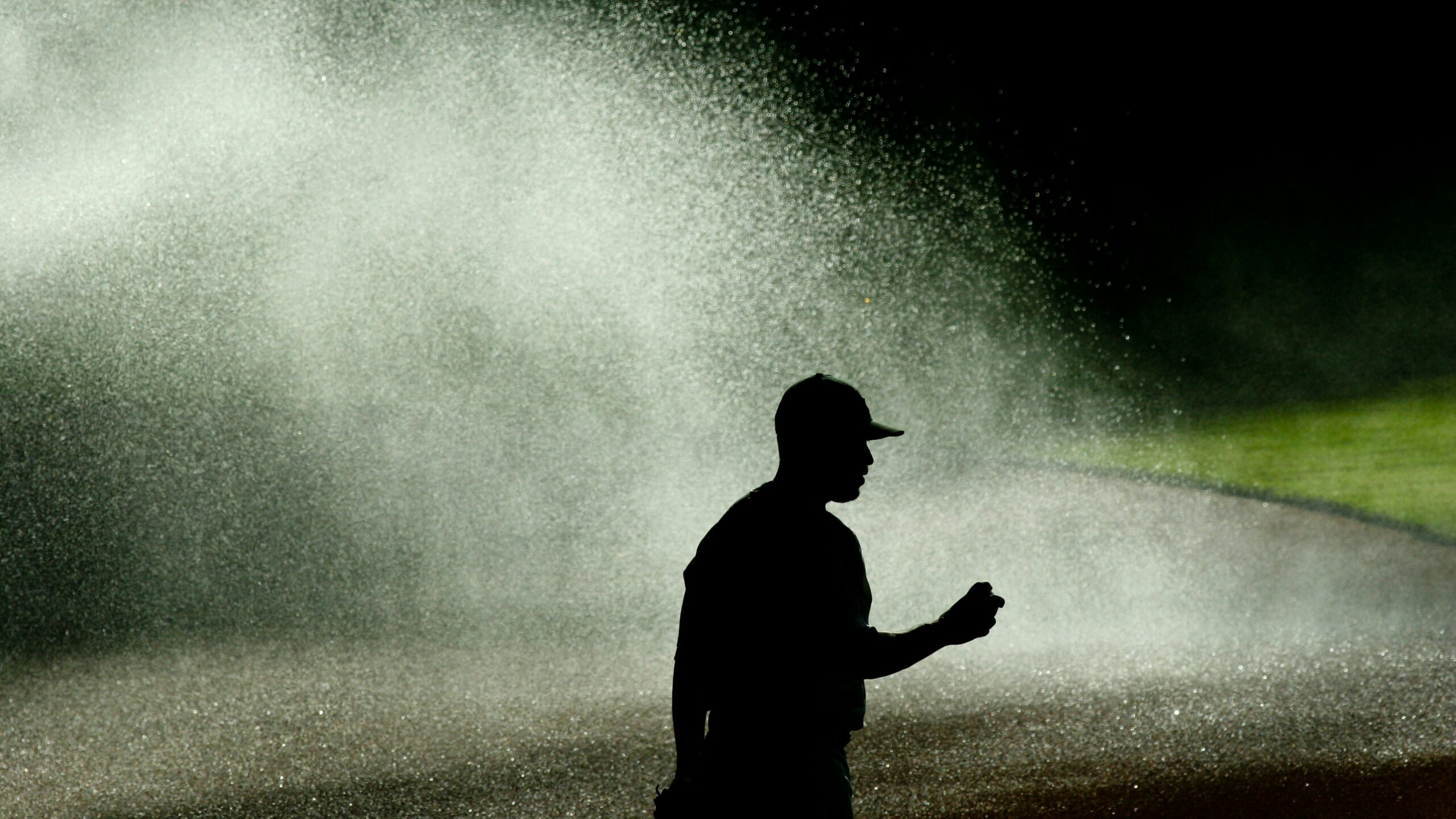 Silhouette of a pitcher on a baseball field with the sprinkler on behind him.