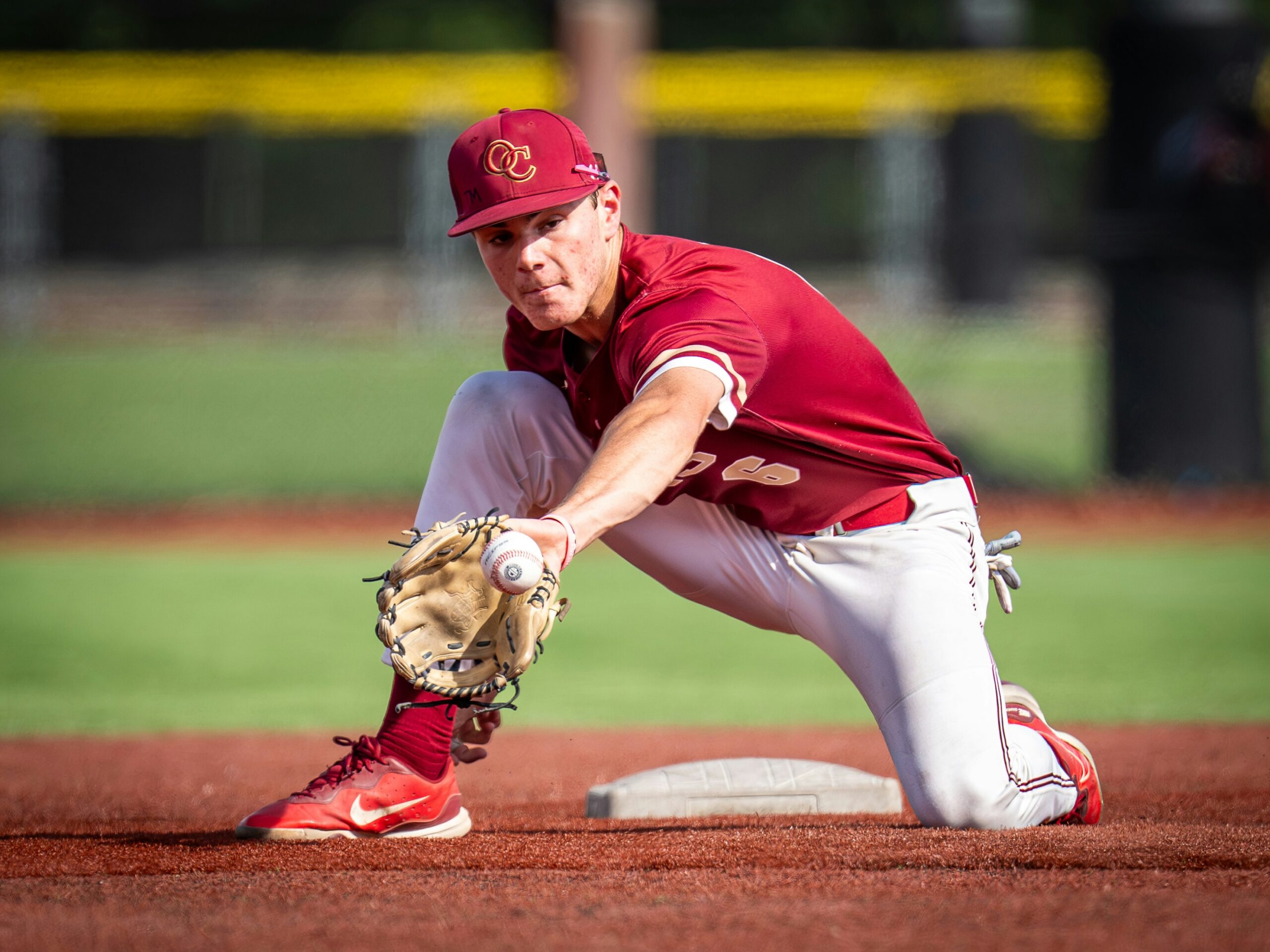 An infield baseball player reaches down with his mitt to catch the ball.