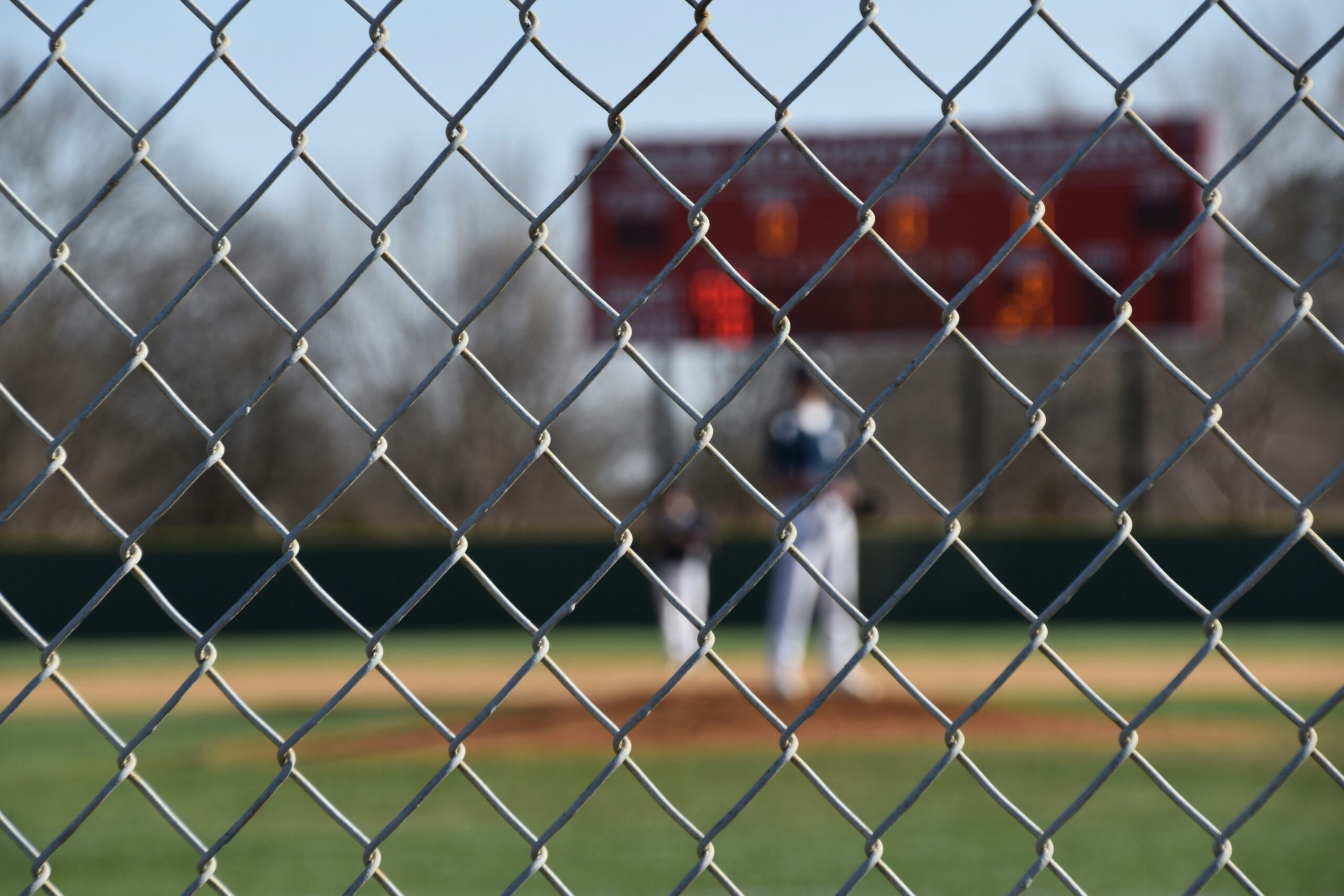 A chain link fence partially obscures the view of a baseball field.
