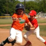 A baseball player is running toward a base, while the player behind him is catching the ball.