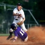 A baseball player slides into base in a cloud of dust.
