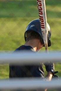 A baseball player holds his bat while looking at the ground.