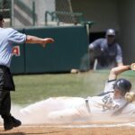 A base runner slides into place while the umpire gestures at him.