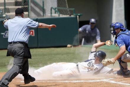 A base runner slides into place while the umpire gestures at him.