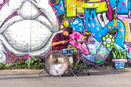 A musician performs in front of a brightly colored wall mural.