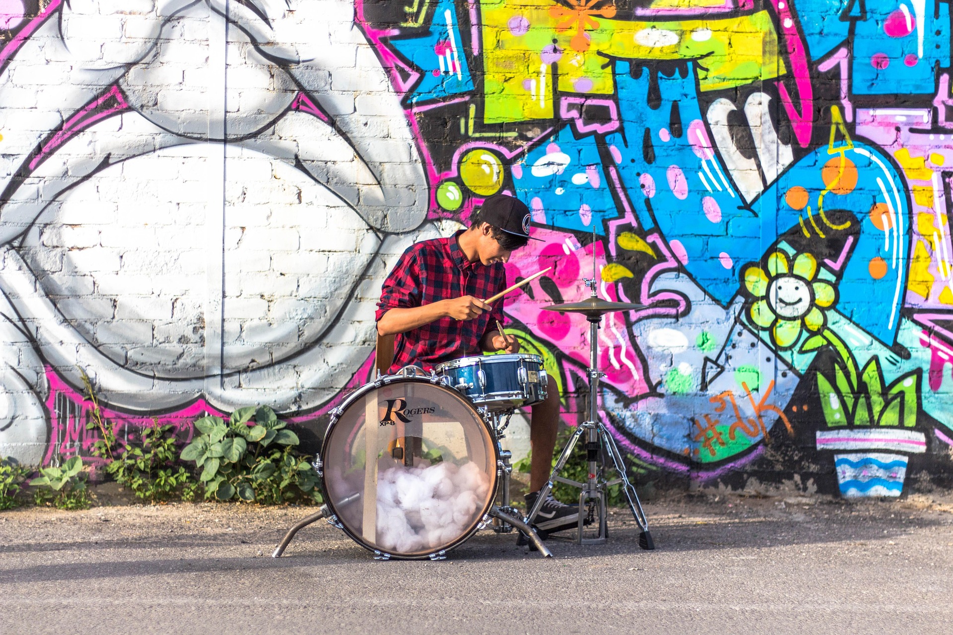 A musician performs in front of a brightly colored wall mural.