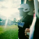 A baseball player is in the dugout with the sun behind him.