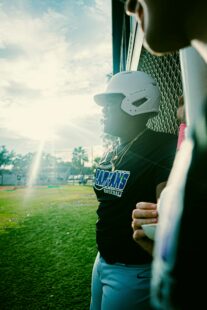 A baseball player is in the dugout with the sun behind him.