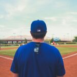 A man wearing a blue baseball cap is facing a baseball field.