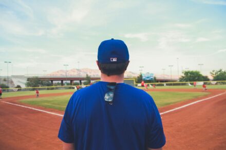 A man wearing a blue baseball cap is facing a baseball field.