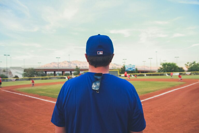 A man wearing a blue baseball cap is facing a baseball field.