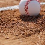 A new baseball is resting in the dirt on a baseball field.