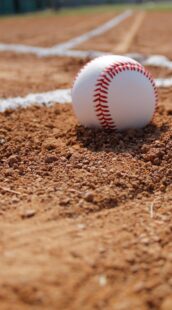 A new baseball is resting in the dirt on a baseball field.