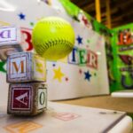 A neon green baseball collides with a stack of baby blocks.