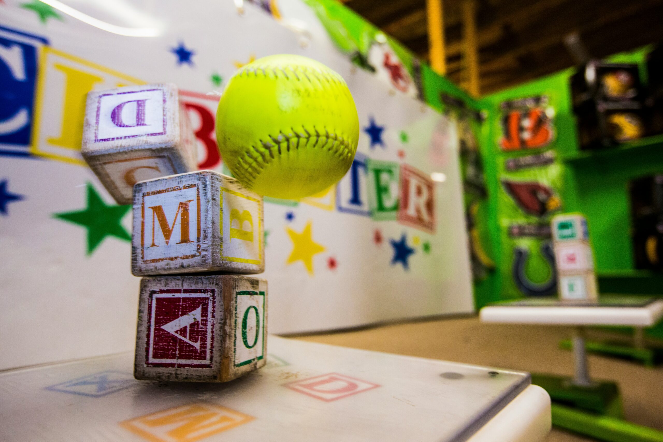 A neon green baseball collides with a stack of baby blocks.