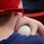 A child in a baseball cap holds a baseball to their shoulder.
