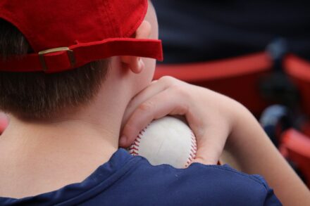 A child in a baseball cap holds a baseball to their shoulder.