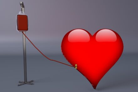 Red heart connected to a blood donation bag and IV stand by a tube, symbolizing blood donation and lifesaving care.