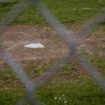 Through a chain-link fence, an empty home plate is visible.