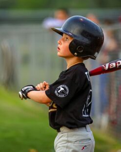 A baseball player holding hit bat looks up in anticipation.
