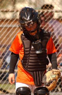 A baseball catcher looks sadly at the ground.