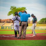 A baseball player scuffs at home plate with the catcher and umpire standing nearby.