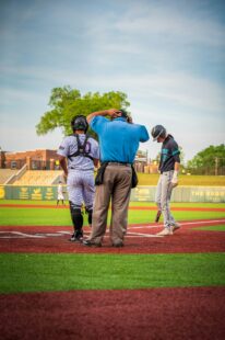 A baseball player scuffs at home plate with the catcher and umpire standing nearby.