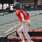 A baseball player follows the ball with his eyes as he gets ready to run.
