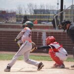 A batter at home plate swings, while the catcher and umpire crouch behind him.
