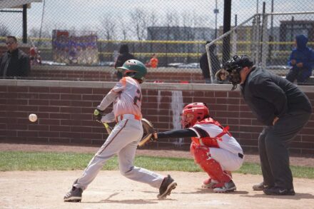 A batter at home plate swings, while the catcher and umpire crouch behind him.