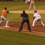 A player looks to steal third base while the umpire crouches nearby.