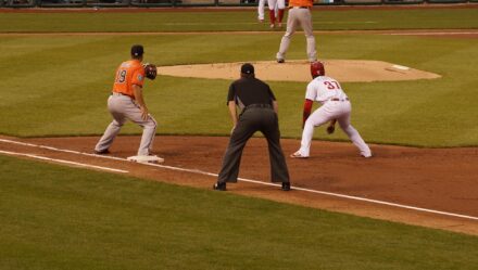 A player looks to steal third base while the umpire crouches nearby.