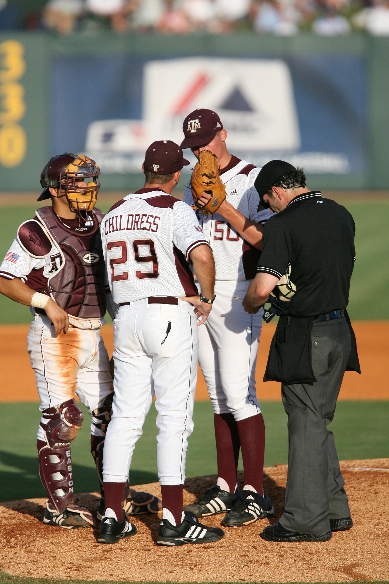 Coach, catcher, umpire, and pitcher gather on the mound during a baseball game.