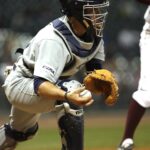 A catcher leans forward to catch the ball.