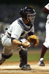 A catcher leans forward to catch the ball.