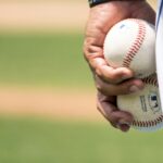 A pitcher holds two baseballs in his left hand.