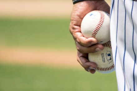 A pitcher holds two baseballs in his left hand.
