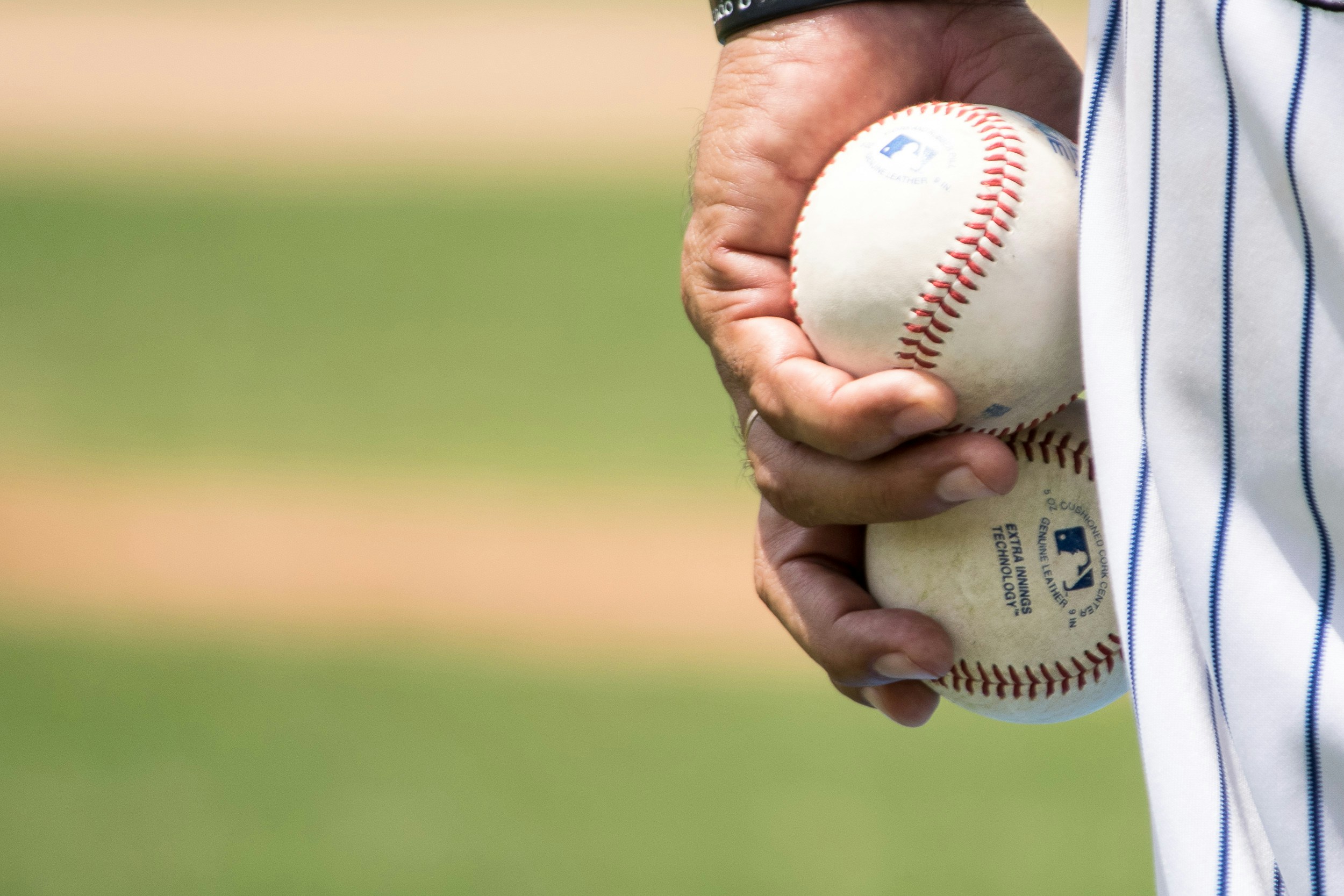 A pitcher holds two baseballs in his left hand.