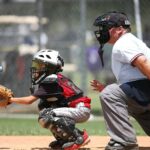 The catcher is crouched behind home plate, with the umpire looking on.