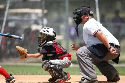 The catcher is crouched behind home plate, with the umpire looking on.