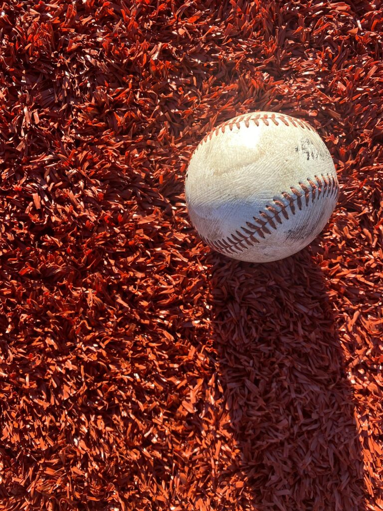 A baseball sits atop a spread of red mulch.