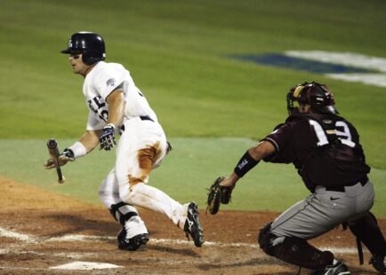 A baseball player begins running to first while dropping his bat.